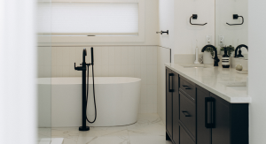 Modern minimalist bathroom interior featuring a white freestanding bathtub, matte black floor-mounted faucet, and dark vanity with a white marble countertop.